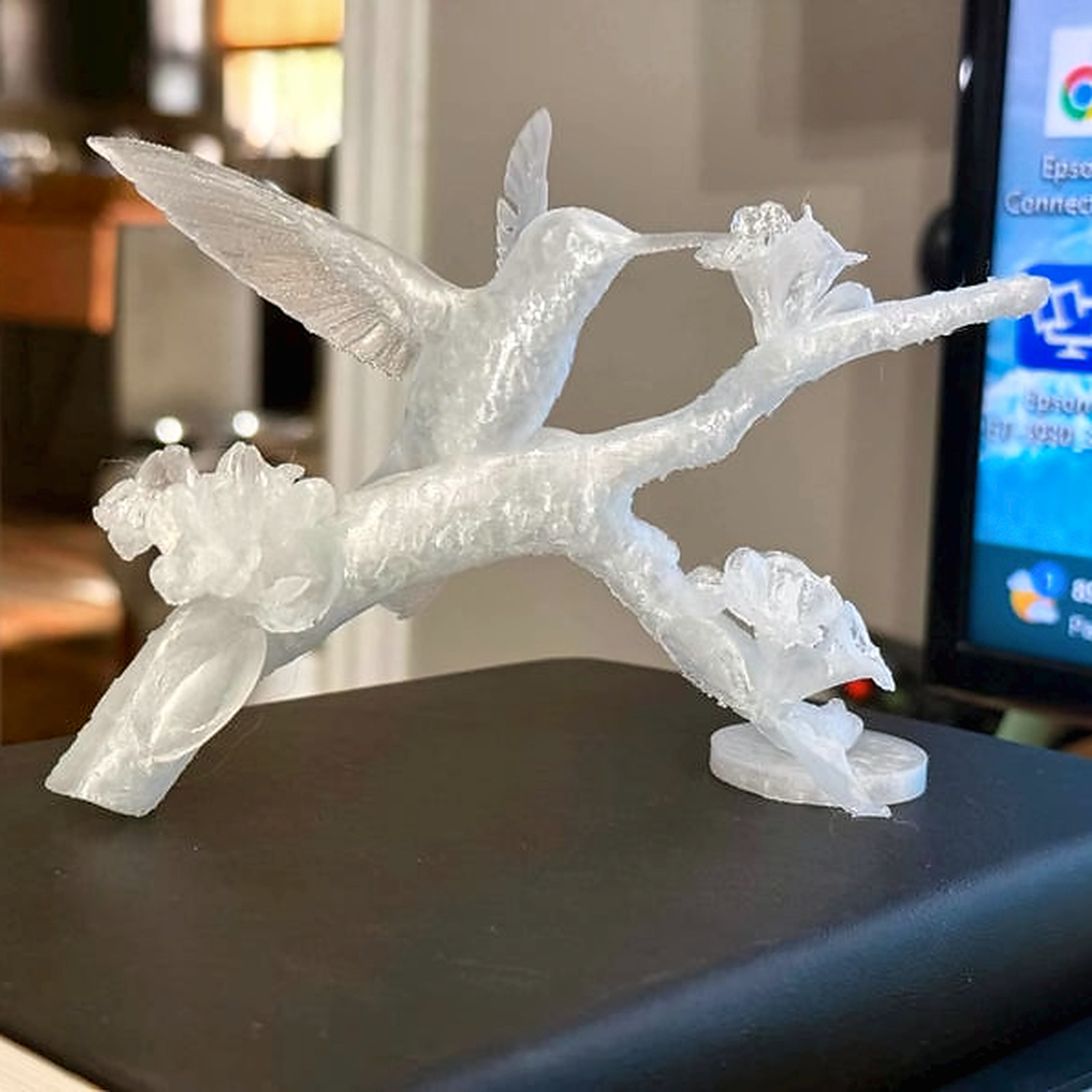 Translucent clear hummingbird figurine on a branch with pale blossoms.
